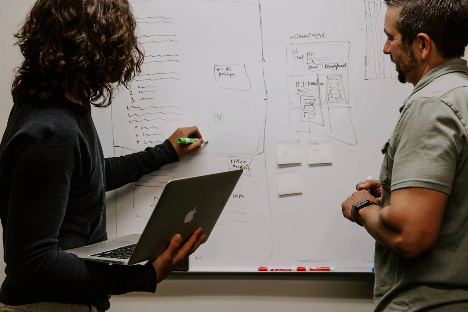 Woman writing on whiteboard with laptop in her hands
